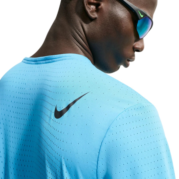 En person iført en lyseblå Nike AeroSwift løbetrøje med korte ærmer, Herre (Lt Current Blue/Black), og reflekterende solbriller ses bagfra og fra siden, hvilket fremhæver det sorte Nike-logo på den øverste del af skulderen.