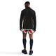 En person står med front mod kameraet iført en sort Nike Nk Df Jakob Hz langærmet skjorte til mænd, flerfarvede sportsshorts, sorte knæstrømper og sorte sportssko på en hvid baggrund.