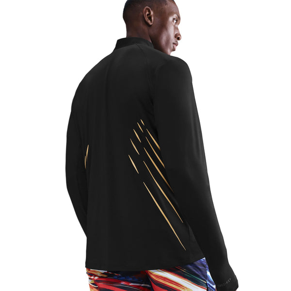 En person står med ryggen til kameraet i en Nike Nk Df Jakob Hz, Herre, Sort langærmet jakke med gulddiagonale striber på ryggen og farverige mønstrede shorts mod en hvid baggrund.
