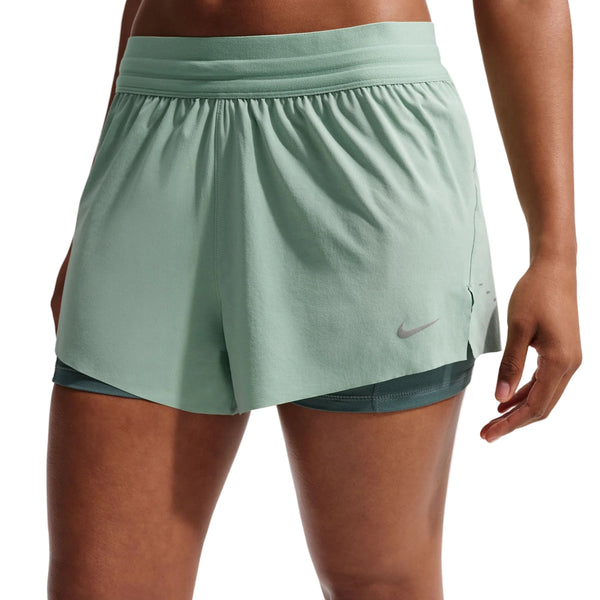En person er iført Nike Nk Swift Df Mr 2N1 Shrt dame løbeshorts i Steam/Mineral Slate/Reflective Silver med et diskret logo på venstre ben og Dri-FIT-teknologi. Kun underkroppen og overbenene er synlige mod en ensfarvet baggrund.