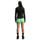 En person står med ryggen til og er iført en sort langærmet bluse, Nike Swift Mid-Rise 2-i-1-løbeshorts til kvinder i farven Illusion Green/Reflective Silver med Dri-FIT-teknologi, sorte sokker og sorte sko. Baggrunden er ensfarvet hvid. Personens hår er sat op i lange fletninger.