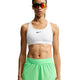 En person står med ansigtet vendt fremad foran en hvid baggrund og er iført en hvid Nike-sport-bh, Nike Swift Mid-Rise 2-i-1-løbeshorts til kvinder i farven Illusion Green/Reflective Silver med Dri-FIT-teknologi samt rødtonede sportsolbriller.
