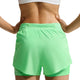 Der ses en person set bagfra med hænderne på hofterne, iført en hvid sports-BH og Nike Swift Mid-Rise 2-i-1-løbeshorts i damemodel, farven Illusion Green/Reflective Silver. Disse løbeshorts har et lagdelt design, Dri-FIT-teknologi til fugtregulering og en lille lomme med lynlås i linningen.