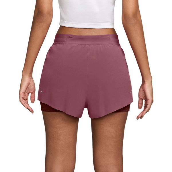 Der ses en person fra livet og ned, iført en hvid, kort top sammen med Nike Swift Mid-Rise 2-i-1-løbeshorts til kvinder i farvekombinationen Pink Smoke/Mystic Dates/Reflective Silver. Bagsiden fremhæver shortsenes elastiske linning og slidser i siderne samt et lagdelt design inspireret af Nike Swift-shortsene, der øger komforten og bevægelsesfriheden.
