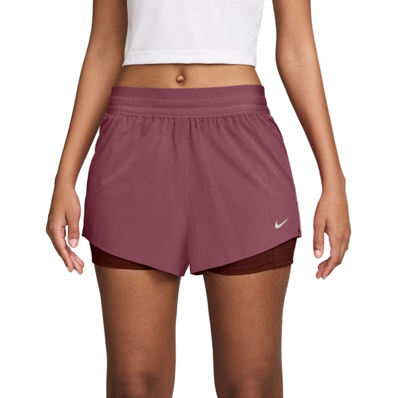 En person har en hvid crop top på samt Nike Swift Mid-Rise 2-i-1-løbeshorts til kvinder i farvekombinationen Pink Smoke/Mystic Dates/Reflective Silver, der har et dobbeltlagsdesign med Dri-FIT-teknologi – perfekt til træning. Billedet er beskåret fra skuldrene til midt på låret og viser det ikoniske Nike-logo nær den nederste højre kant af disse løbeshorts.