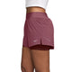 En person ses fra livet og ned i profil mod en ensfarvet baggrund, iført Nike Swift Mid-Rise 2-i-1-løbeshorts til kvinder i farvekombinationen Pink Smoke/Mystic Dates/Reflective Silv samt en hvid top. Shortsene er udstyret med Dri-FIT-teknologi, Nike-logoet og en lille slids i siden.