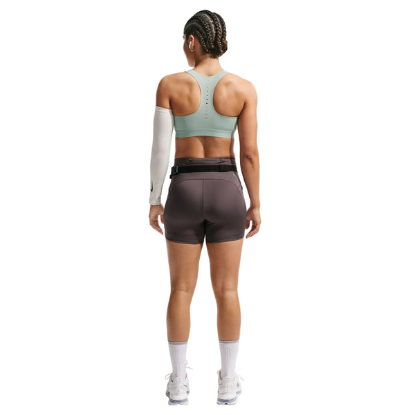 En person står med ryggen til, iført en Nike Nk Swift Hs Bra til kvinder i Steam/Reflective Silver, mørkegrå shorts, hvide sokker, løbesko; håret er flettet, med et ærme og et bælte - klar til højintensiv træning.