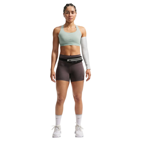 En kvinde kigger frem i en Nike Nk Swift Hs Bra, Dame, Steam/Reflective Silv - sammen med brune sportsshorts, et hvidt ærme på venstre arm, hvide knæstrømper, hvide sko og en sort taljepose - ideel til højintensiv træning.