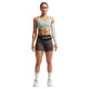 En kvinde kigger frem i en Nike Nk Swift Hs Bra, Dame, Steam/Reflective Silv - sammen med brune sportsshorts, et hvidt ærme på venstre arm, hvide knæstrømper, hvide sko og en sort taljepose - ideel til højintensiv træning.
