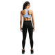 En kvinde står med ryggen til og har en lyseblå Nike High-Support Lightly Lined sports-BH til kvinder i farven Aluminium/Reflective Silver på, sorte leggings og sorte sportssko. Hendes hår er sat op i fletninger, og hun står foran en ensfarvet hvid baggrund.