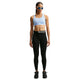 En person står med ansigtet vendt fremad og er iført en Nike High-Support Lightly Lined sports-BH til kvinder i farven Aluminium/Reflekterende Sølv, sorte leggings, sorte sneakers, en bæltetaske, blå solbriller og har langt flettet hår. Baggrunden er ensfarvet hvid.