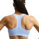 Der ses en person med flettet hår set bagfra, iført Nike High-Support Lightly Lined Sports Bra til kvinder i farven Aluminium/Reflekterende Sølv. Denne sports-BH med høj støtte har små ventilationshuller, der løber ned ad midten af ryggen, og er udstyret med Dri-FIT-teknologi, der hjælper med at holde dig kølig og tør. Personens arme er let løftet.