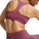 En person sidder set bagfra iført en lyserød Nike High-Support Lightly Lined Sports Bra med innovativ Dri-FIT-teknologi og matchende sportsshorts med Nike-logoet. Billedet fremhæver pasformen, det avancerede materiale og designet i dette sportstøj fra Dame-kollektionen.