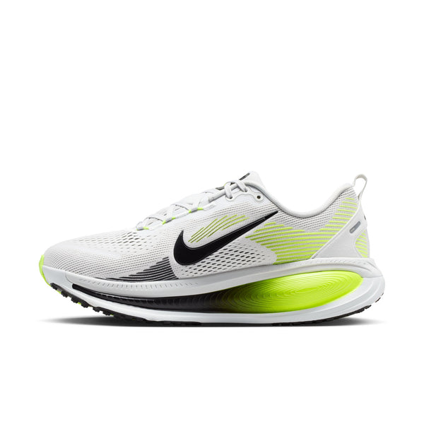 Nike Vomero 18 til mænd i farvekombinationen Photon Dust/Black-Volt har en hvid overdel i mesh med sorte og neongule detaljer, herunder et sort Nike Swoosh-logo. Denne løbesko er designet med henblik på maksimal støddæmpning, komfort og ydeevne og vises her set fra siden, hvor den buede, støddæmpende sål fremhæves.
