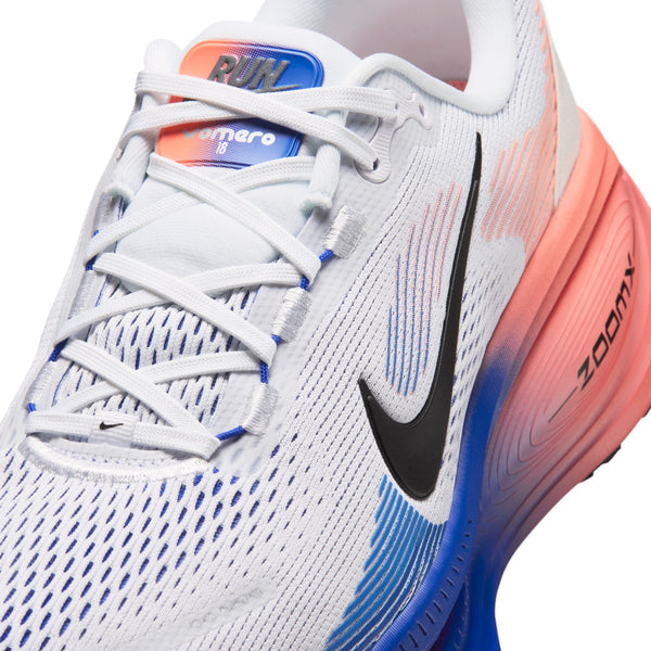 Nærbillede af et par hvide Nike Vomero 18 herreløbesko med et sort Nike-swoosh, racerblå mesh-detaljer ved tåen og en hæl i en farveovergang fra atomrosa til orange. De synlige snørebånd og »ZoomX«-logoet på siden understreger maksimal komfort ved hvert skridt.
