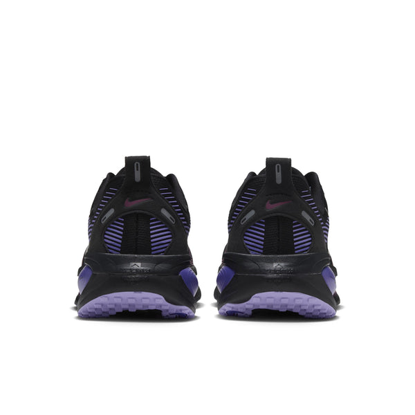 Her ses et par Nike Vomero 18 løbesko til kvinder i farven Black/Metallic Silver set bagfra, med diskrete metalliske sølvdetaljer og et lille Nike-logo øverst på hver sko. Disse sko er designet til maksimal dæmpning og giver enestående komfort og støtte ved hvert skridt.
