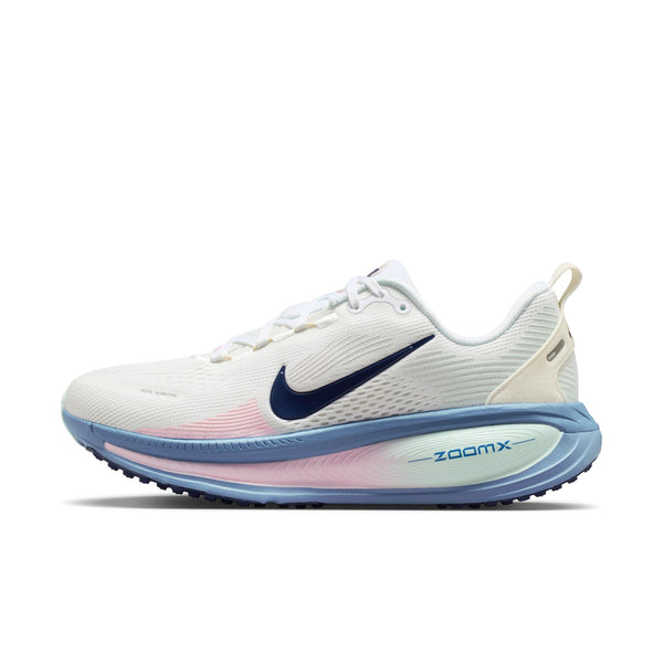 Nike Vomero 18 Dame-løbeskoen i farvekombinationen White/Midnight Navy-Work Blue har maksimal støddæmpning, et marineblåt Swoosh-logo, en lyseblå sål, ZoomX-mærkning på mellemsålen, en diskret lyserød farveovergang nær mellemsålen, hvide snørebånd og en beige hælflap.