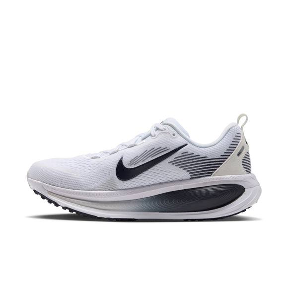 En hvid Nike Vomero 18-løbesko til kvinder, vist fra siden mod en ensfarvet hvid baggrund, med et sort Swoosh-logo, sorte og grå detaljer, hvide snørebånd, åndbart mesh-overmateriale samt en tyk hvid og sort sål designet til maksimal dæmpning. Farvekombinationen er WHITE/GRIDIRON-PHOTON DUST-PHANTOM.