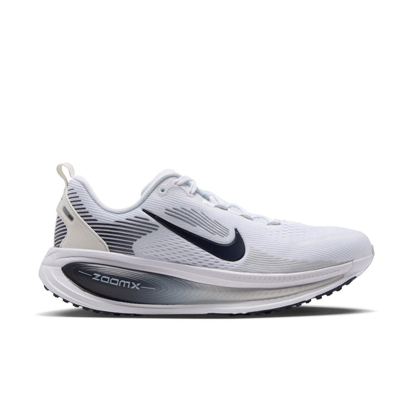 En Nike Vomero 18 damesko i farvekombinationen WHITE/GRIDIRON-PHOTON DUST-PHANTOM har et sort Nike Swoosh-logo, grå og sorte detaljer på hælen, ZoomX-mærkning på mellemsålen, der sikrer maksimal dæmpning, samt en åndbar overdel i mesh. Skoen vises set fra siden på en ensfarvet hvid baggrund.