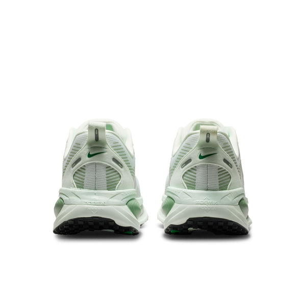 Et par Nike Vomero 18 Dame-sneakers i Barely Green/Metallic Silver-Steam er vist bagfra på en hvid baggrund med små grønne Nike-logoer på hver hæl og sorte gummisåler for maksimal dæmpning.