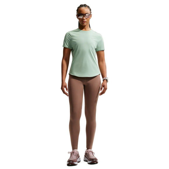 En kvinde står med ansigtet fremad iført en lysegrøn Nike Swift SS Running Top, Dame, Steam/Reflective Silv, taupefarvede leggings, lilla sportssko, solbriller og et ur. Den åndbare løbetop fremhæver komfort og stil mod den hvide baggrund.