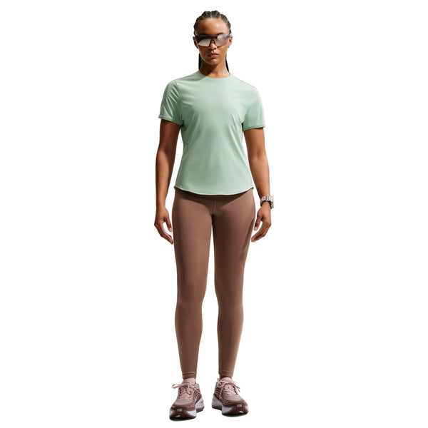 En kvinde står med ansigtet fremad iført en lysegrøn Nike Swift SS Running Top, Dame, Steam/Reflective Silv, taupefarvede leggings, lilla sportssko, solbriller og et ur. Den åndbare løbetop fremhæver komfort og stil mod den hvide baggrund.