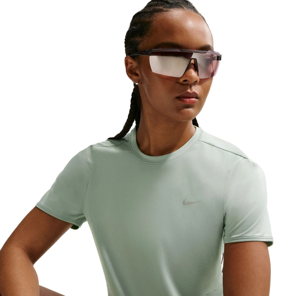 En person med flettet hår bærer store reflekterende solbriller og en lysegrøn Nike Swift SS Running Top, Dame, Steam/Reflective Silv-an åndbar løbetop - mens han poserer mod en hvid baggrund.