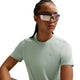 En person med flettet hår bærer store reflekterende solbriller og en lysegrøn Nike Swift SS Running Top, Dame, Steam/Reflective Silv-an åndbar løbetop - mens han poserer mod en hvid baggrund.