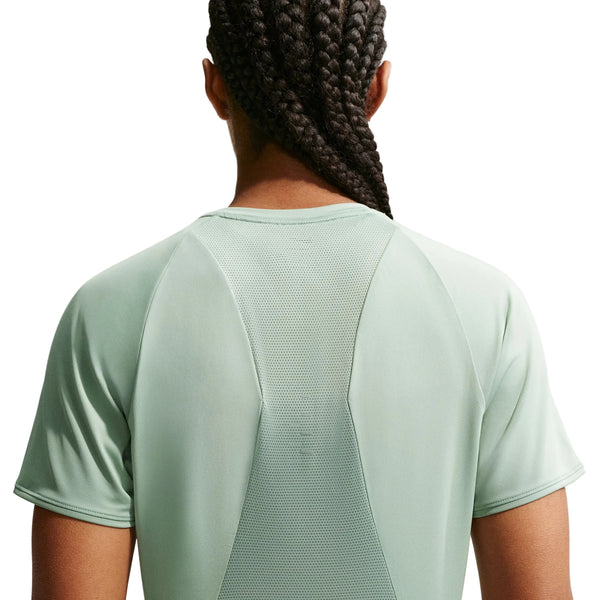Billedet viser bagsiden af en person med lange fletninger iført en lysegrøn Nike Swift SS Running Top, Dame, Steam/Reflective Silv. Mesh-paneler giver ventilation, hvilket gør den ideel til at holde sig afkølet under løb. Baggrunden er almindelig hvid.