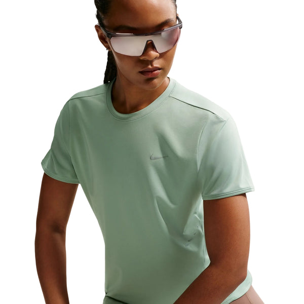 En person iført reflekterende solbriller og en lysegrøn Nike Swift SS Running Top, Dame, Steam/Reflective Silv - en åndbar teknisk løbetrøje kvinder - kigger ud til siden mod en almindelig hvid baggrund.