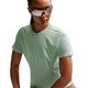 En person iført reflekterende solbriller og en lysegrøn Nike Swift SS Running Top, Dame, Steam/Reflective Silv - en åndbar teknisk løbetrøje kvinder - kigger ud til siden mod en almindelig hvid baggrund.