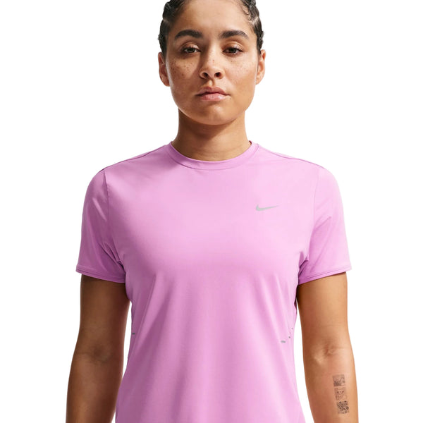 En kvinde med mørkt hår, der er bundet tilbage, bærer Nike Swift SS Running Top, Dame i Lt Magenta/Reflective Silv - en fugttransporterende top, der er ideel til enhver løbegarderobe - mens hun ser fremad med et neutralt udtryk mod en almindelig hvid baggrund.