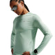 En kvinde i Nikes Swift UV Long Sleeve Shirt til kvinder, i Steam/Reflective Silver, med lynlåslomme og spejlsolbriller står med hænderne på hofterne mod en ensfarvet baggrund.