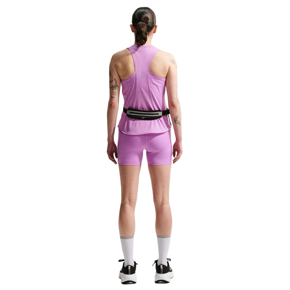 En person står med ryggen til og er iført en Nike Nk Swift Df Tank Top, Dame i Lt Magenta/Reflective Silv med matchende shorts, lange hvide sokker, hvide sneakers og en taljetaske. Tatoveringer dækker begge arme, og håret er bundet tilbage for at give et sporty look.