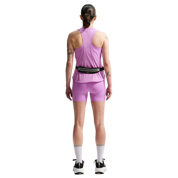 En person står med ryggen til og er iført en Nike Nk Swift Df Tank Top, Dame i Lt Magenta/Reflective Silv med matchende shorts, lange hvide sokker, hvide sneakers og en taljetaske. Tatoveringer dækker begge arme, og håret er bundet tilbage for at give et sporty look.