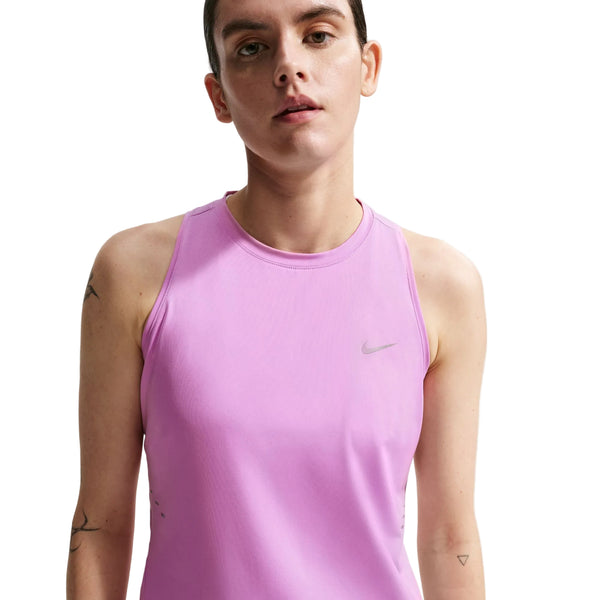 En person med kort brunt hår er iført en ærmeløs, lys magenta Nike Nk Swift Df Tank Top (Dame) med reflekterende sølvdetaljer. Svage tatoveringer på armen er synlige, og baggrunden er helt hvid.