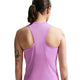 En kvinde med mørkt hår i hestehale ses bagfra iført en ærmeløs Nike Nk Swift Df Tank Top til kvinder i Lt Magenta/Reflective Silv. Tatoveringer er synlige på hendes venstre arm mod en hvid baggrund.