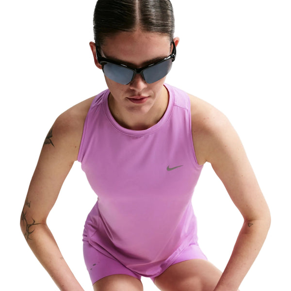 En kvinde i en ærmeløs, lys magenta Nike Nk Swift Df Tank Top, Dame, med reflekterende sølvdetaljer og mørke solbriller kigger nedad. Baggrunden er hvid, og der er et lille Nike-logo på den åndbare top.