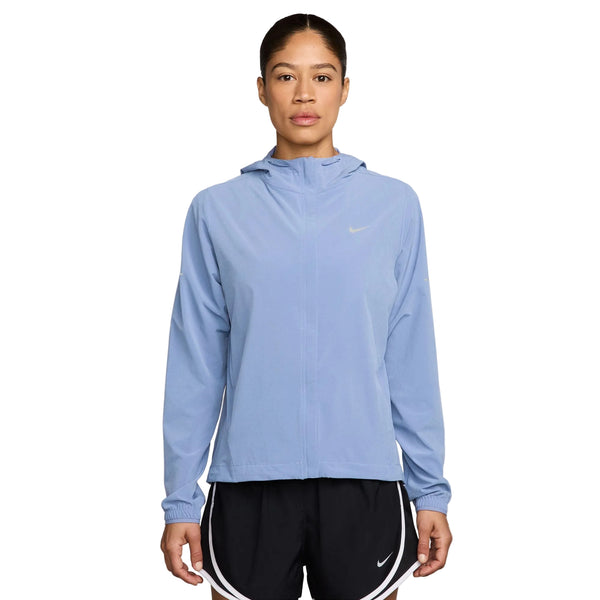 En kvinde står med ansigtet vendt fremad iført en Nike Swift Repel Packable løbejakke til kvinder i farverne aluminium/reflekterende sølv samt sorte sportsshorts med hvid kant. Den lette, vandafvisende jakke er designet med henblik på komfort. Baggrunden er ensfarvet hvid.
