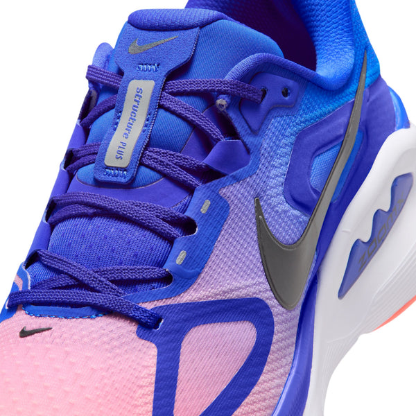 Nærbillede af Nike Structure Plus-løbeskoen til herre i farvekombinationen Racer Blue/Black-Atomic Pink-White, der fremviser en livlig blanding af blå, lyserøde og lilla nuancer. Overdelen i mesh har detaljerede syninger, et gråt Nike-swoosh og et synligt mærke på tungen med teksten »Structure Plus«. Designet med fokus på stabilitet for at støtte løbere, der lider af overpronation.