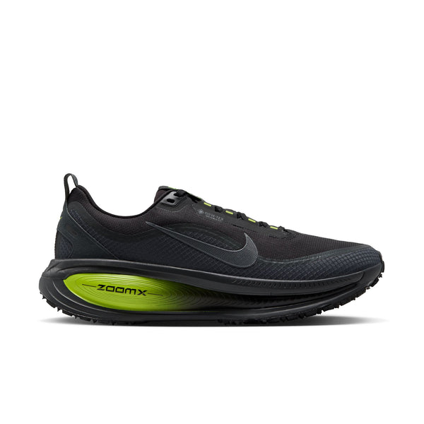 En sort Nike Vomero 18 GORE-TEX-løbesko til mænd med en overdel i antracit og sort med et gråt Nike-swoosh, sorte snørebånd og iøjnefaldende detaljer i Lemon Venom-grøn på ZoomX-mellemsålen. Skoen har en mønstret ydersål og en lav silhuet. Denne model er udviklet som en vandtæt løbesko og tilbyder fremragende ydeevne og beskyttelse til herre-løbesko i al slags vejr. Billedet er taget på en ensfarvet hvid baggrund.
