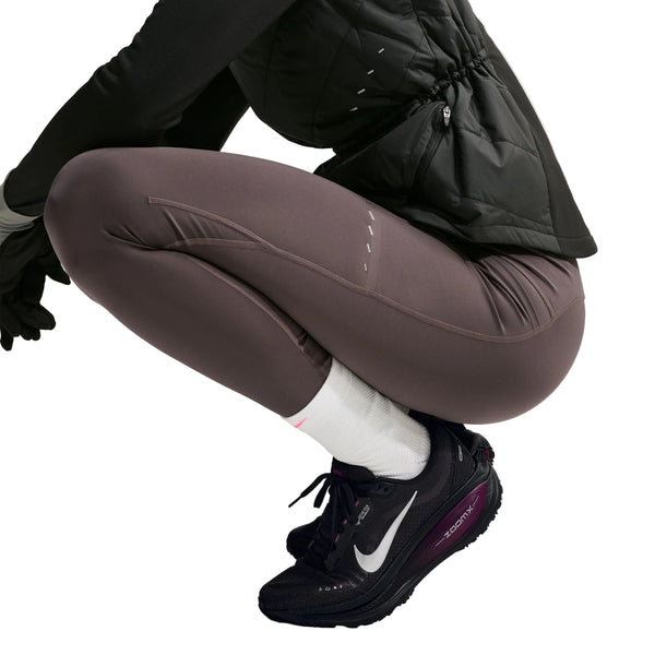 En person iført mørke sportsleggings og Nike Vomero 18 Gore-Tex, Dame, sort/metalsølv-True Berry løbesko sidder på hug foran en ensfarvet baggrund.