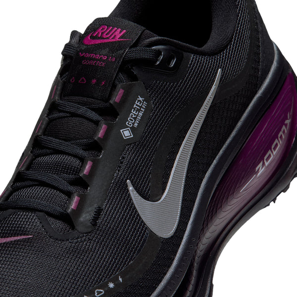 Nærbillede af en Nike Vomero 18 Gore-Tex-løbesko til kvinder i sort og metallisk sølv med detaljer i farven true berry og vandtæt logo på siden.
