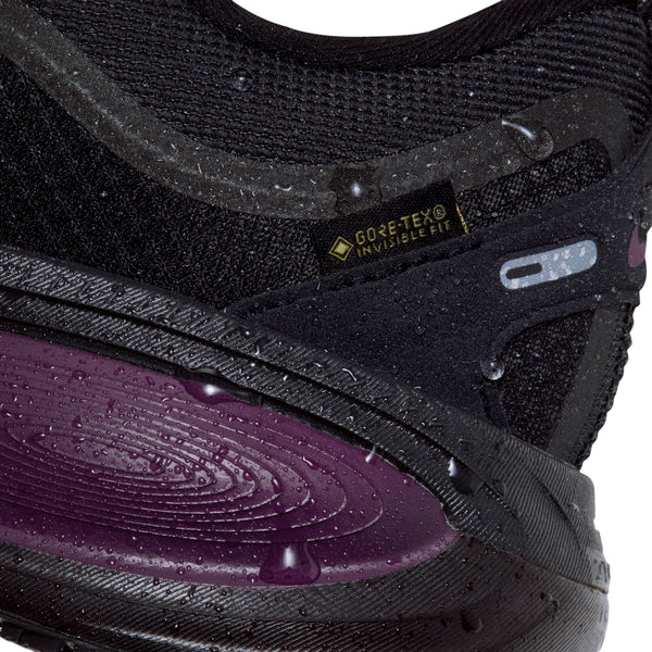 Nærbillede af en sort Nike Vomero 18 Gore-Tex-løbesko med vanddråber, der perler sig på overfladen, og en lilla mellemsål.