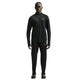 En person står med ansigtet fremad, iført Nike Stride Half Zip Midlayer-løbetrøje til herre i farven Black/Reflective Silv og matchende bukser, suppleret med sorte sko og mørke solbriller. Trøjen er perfekt til herretræning, og Nike-logoet er synligt både på trøjen og bukserne.