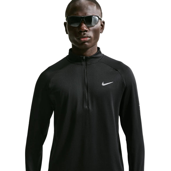 En person iført mørke solbriller og en sort Nike Stride Half Zip Midlayer løbetrøje (Herre, Sort/Reflekterende Sølv) står med ansigtet vendt fremad foran en ensfarvet hvid baggrund og fremviser en elegant herretræningsstil.
