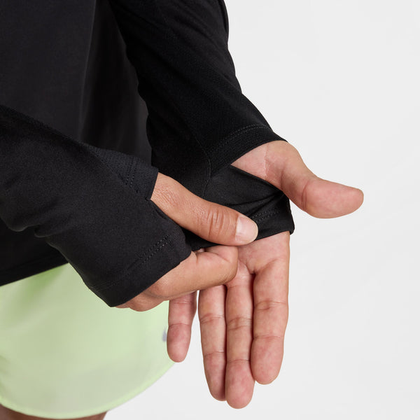 En person, der har en Nike Stride Half Zip Midlayer-løbetrøje i farverne sort/reflekterende sølv og lysegrønne shorts på, retter ærmet over sin venstre hånd foran en ensfarvet hvid baggrund.