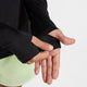 En person, der har en Nike Stride Half Zip Midlayer-løbetrøje i farverne sort/reflekterende sølv og lysegrønne shorts på, retter ærmet over sin venstre hånd foran en ensfarvet hvid baggrund.