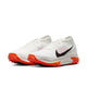 Et par Nike ACG Zegama trailsko til mænd i Summit White/Black-Phantom-Safety Orange med letvægtsdesign, orange såler, sorte swooshes, perforerede detaljer og en Vibram Megagrip-sål, der giver det bedste greb i ujævnt terræn.