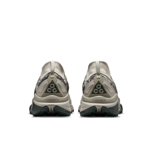 Et par Nike ACG Zegama trail-løbesko til mænd i farvekombinationen Spruce Fog/Black Spruce-Sea Glass-Black ses set bagfra. Hver hæl er forsynet med ACG-logoet, og skoene har Vibram Megagrip-ydersåler med struktur, der er designet til udendørs brug. Baggrunden er ensfarvet hvid.
